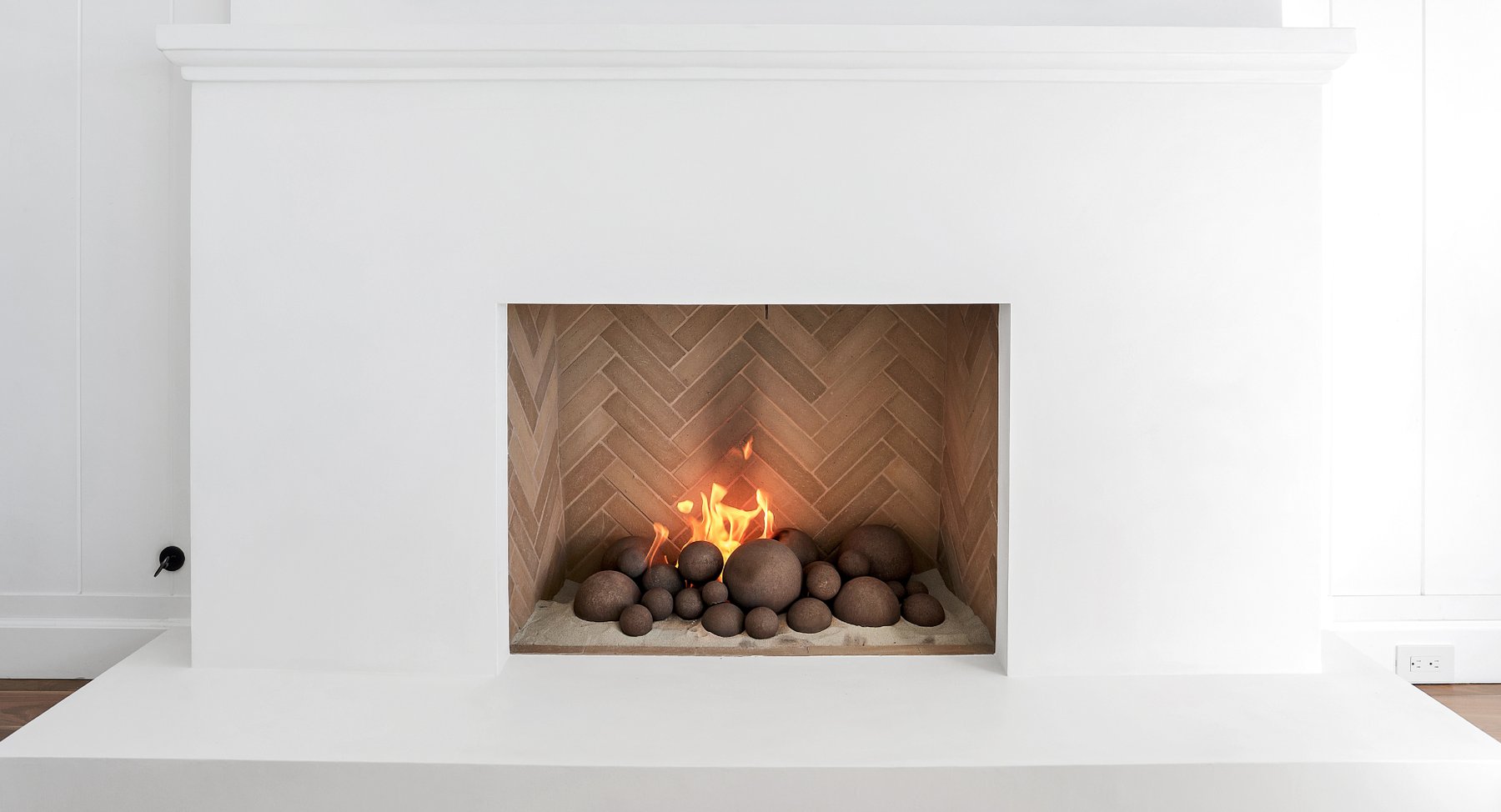 The fireplace after: a smooth white plaster surround and hearth with a herringbone tile firebox and stone fire spheres