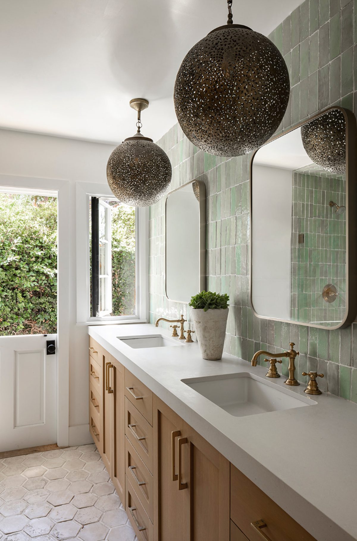 Atelier Azul bath with green zellige tile, an oak double vanity, brass faucets and pierced metal globe pendants