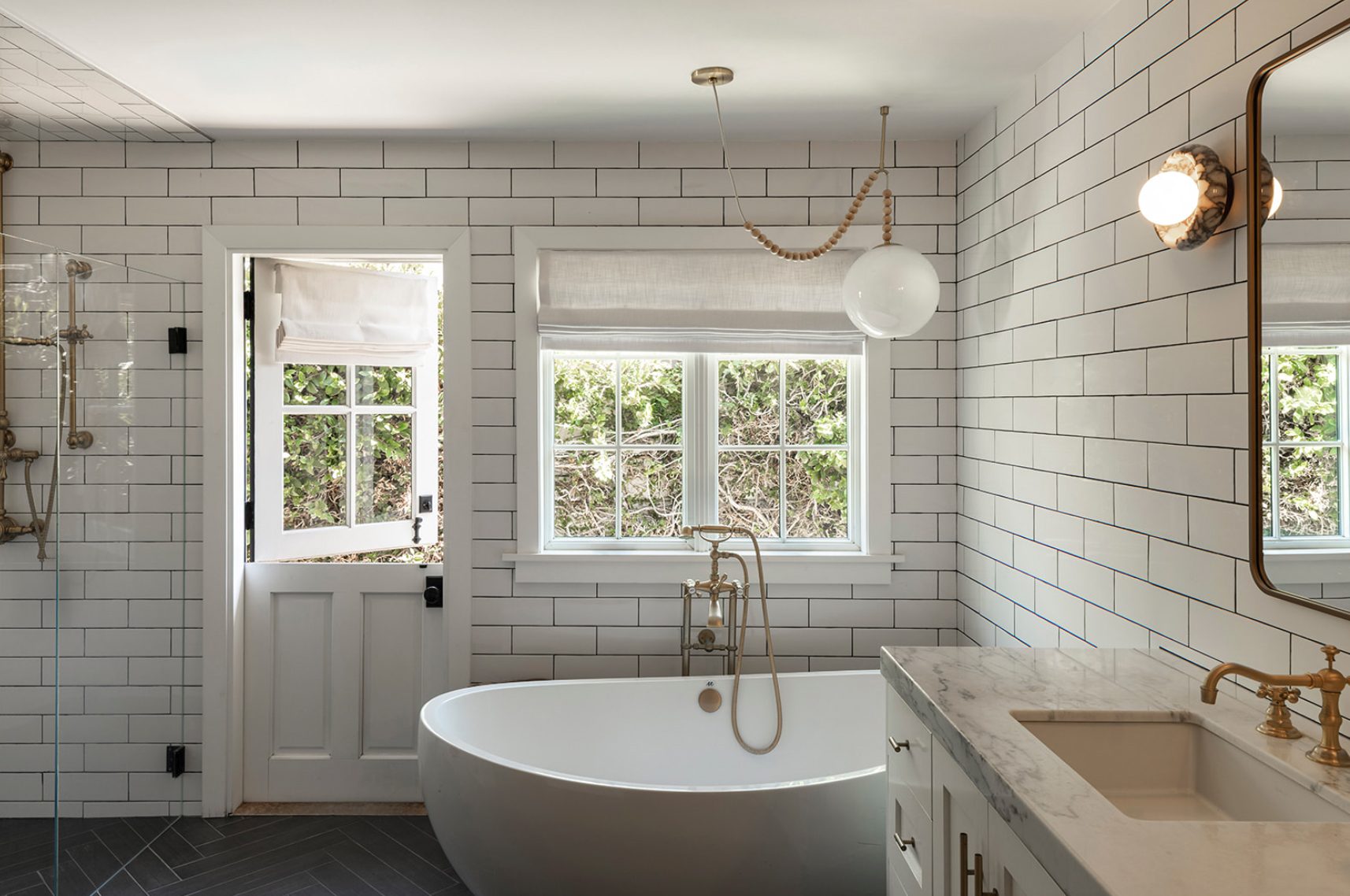 Atelier Azul bath with white subway tile, a freestanding tub, a Dutch door and brass fixtures