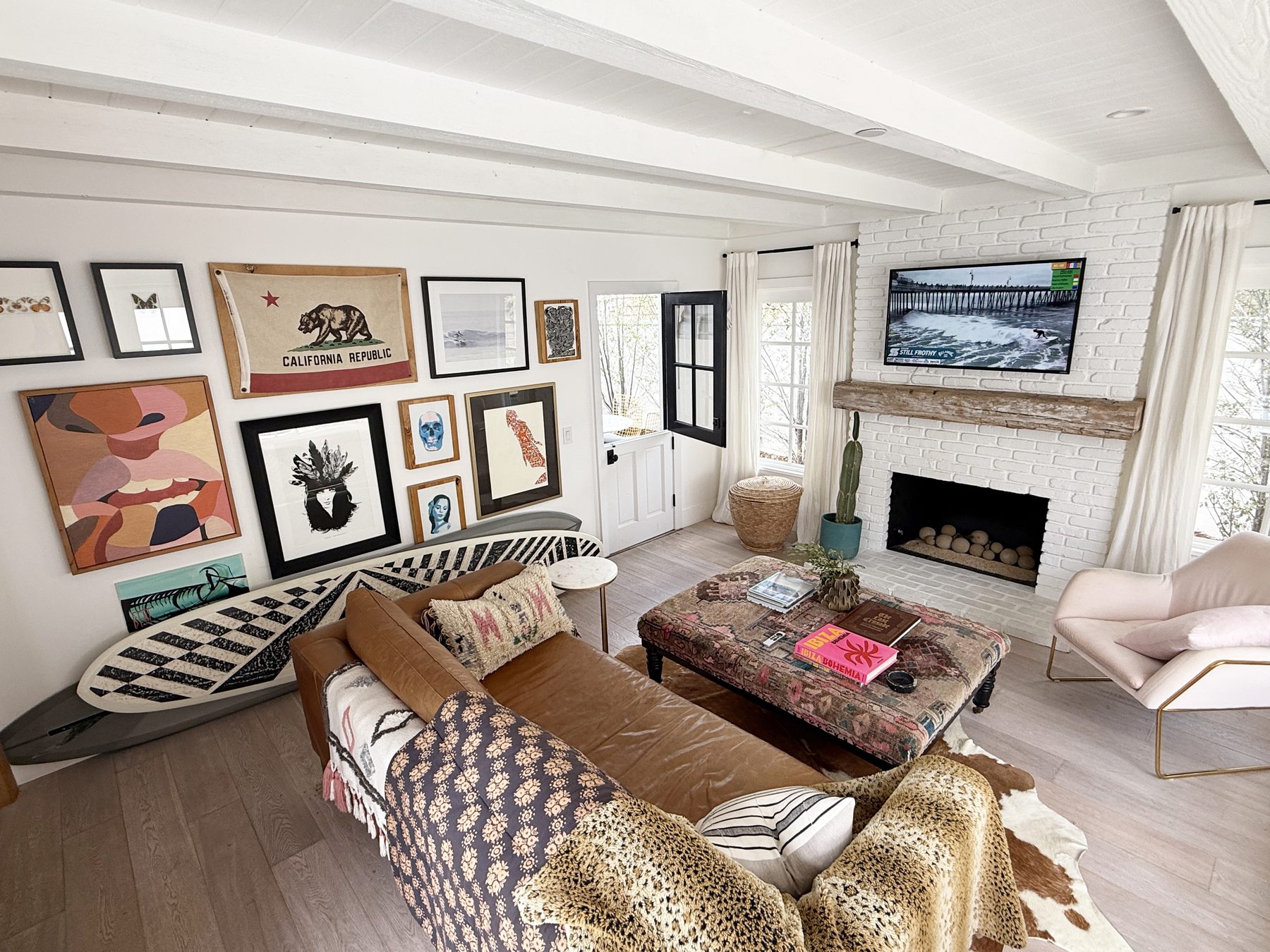 Atelier Azul den with a leather sofa, a white brick fireplace, a gallery wall with a California flag and a patterned surfboard