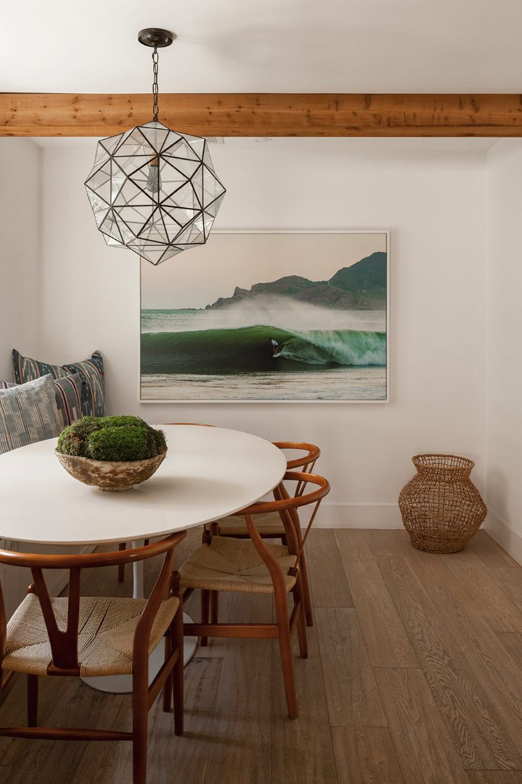 Atelier Azul dining nook with a round white table, wishbone chairs, a faceted glass pendant and a surf photograph