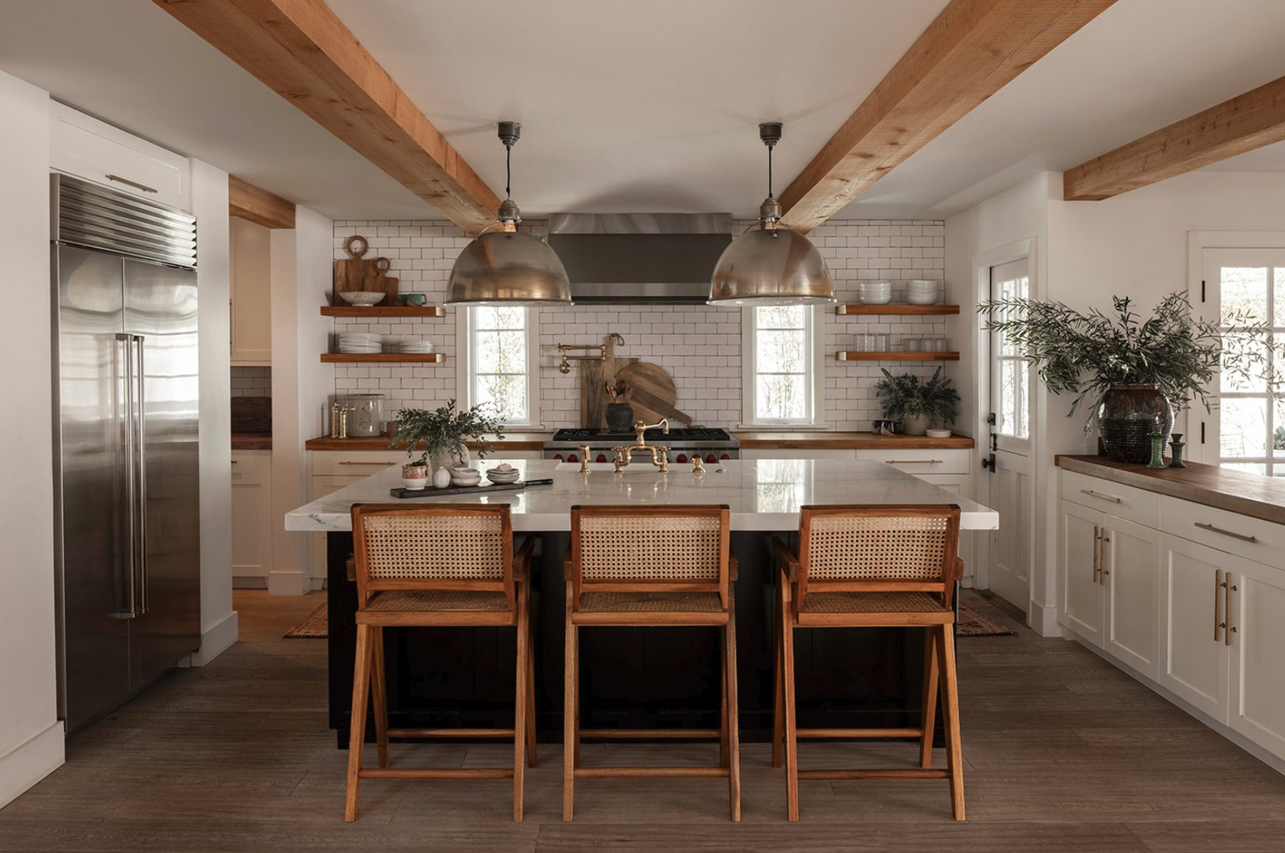 Atelier Azul kitchen with exposed beams, metal dome pendants, a marble island and cane counter stools