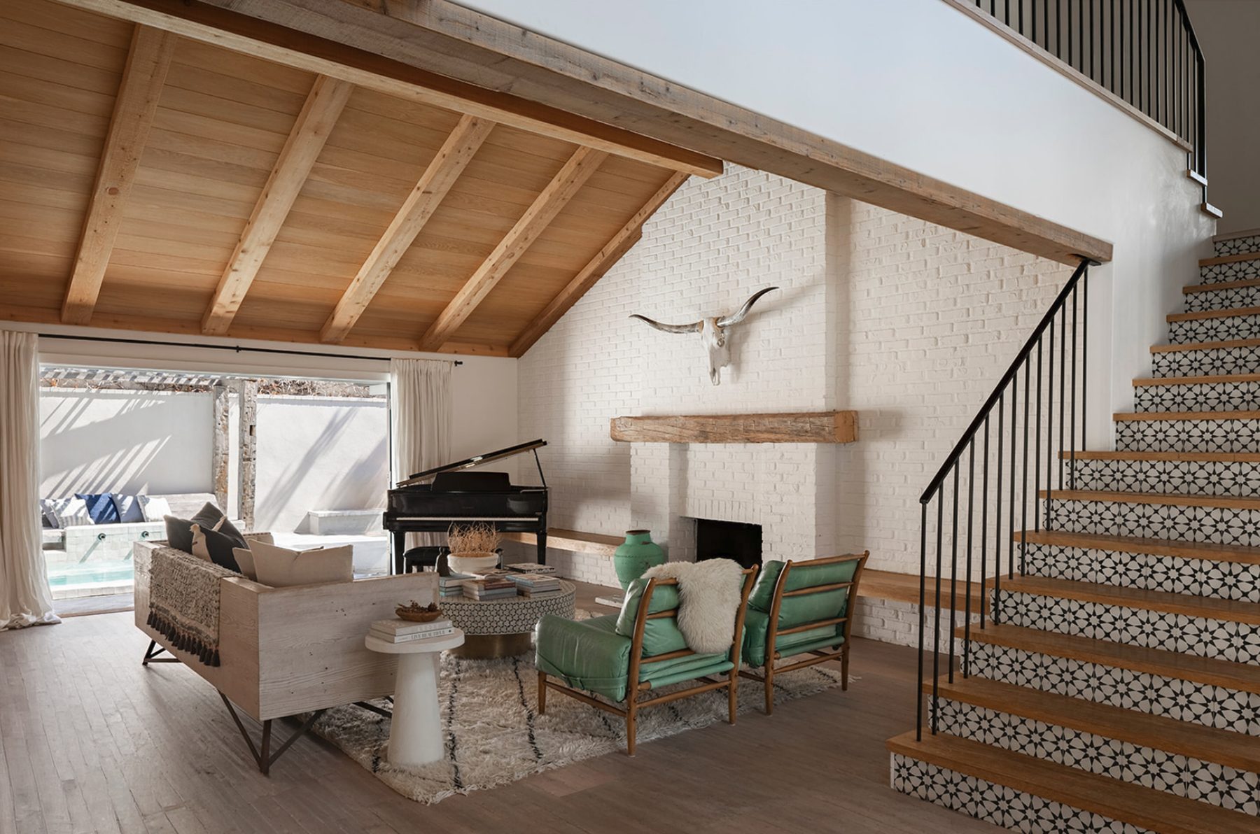 Atelier Azul living room with a beamed wood ceiling, white brick fireplace, green leather chairs, a grand piano and a patterned-tile staircase