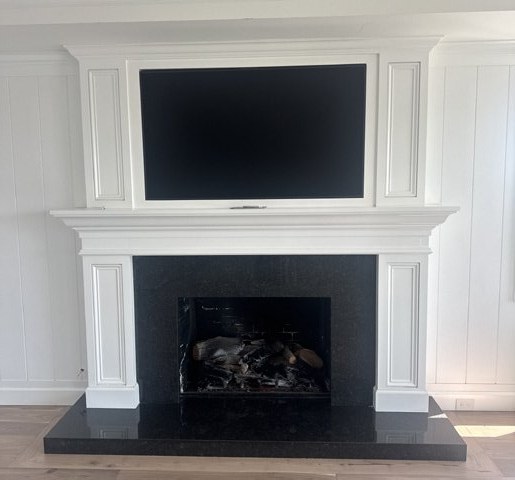 The fireplace before: a white mantel with a television above and a black granite surround and hearth