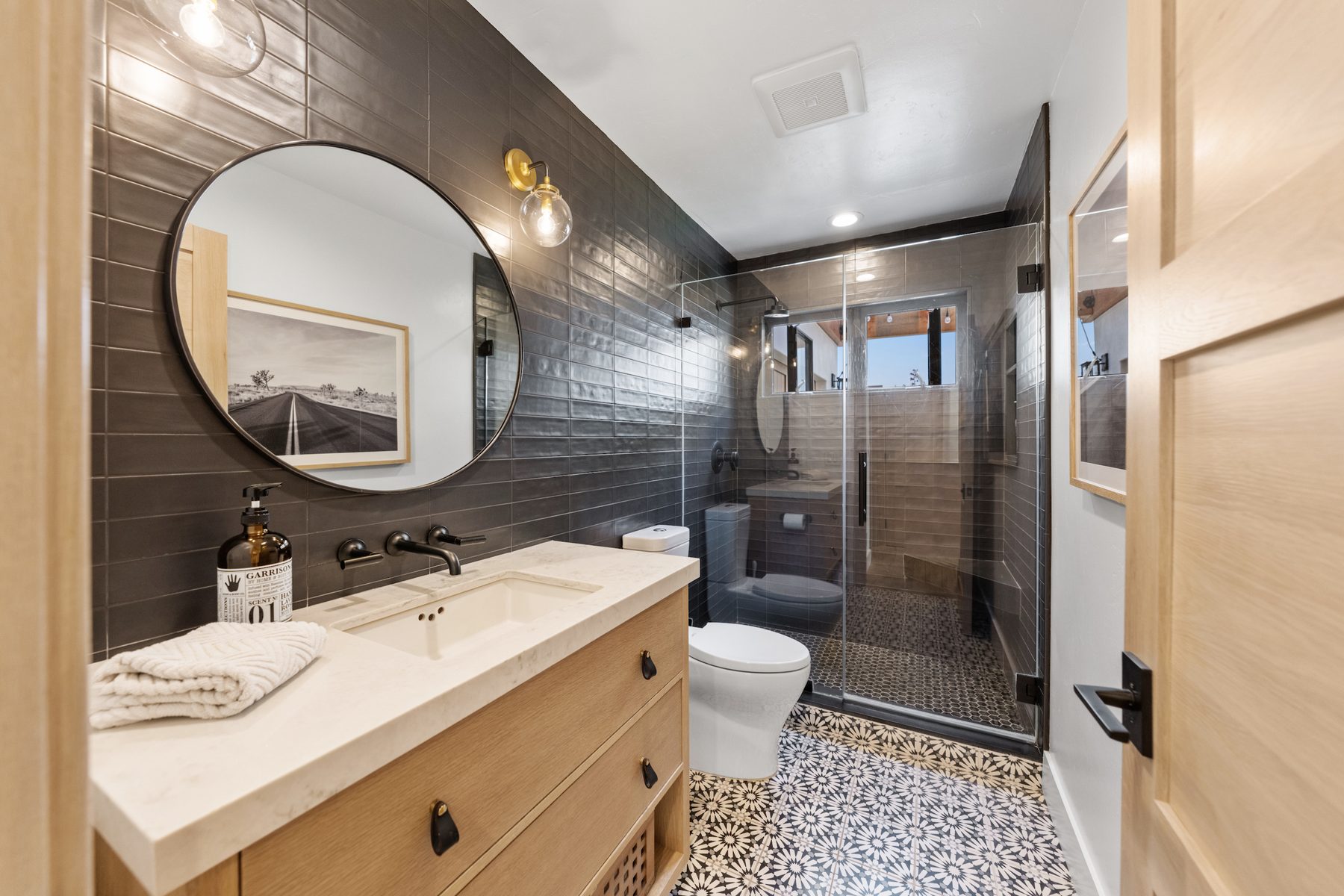 Bath with charcoal glazed tile, a round mirror and a patterned cement tile floor