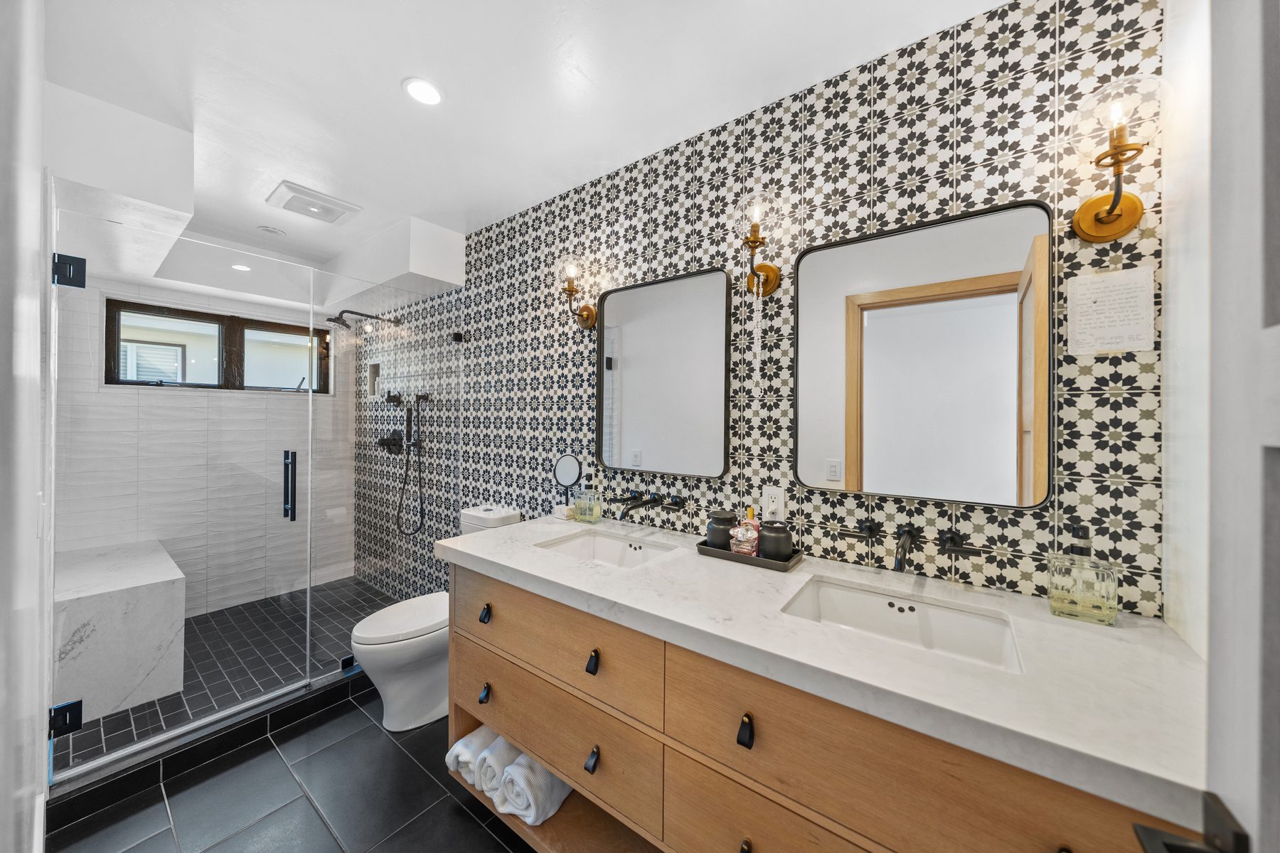 Bath with black and white star-pattern tile, an oak double vanity and brass sconces