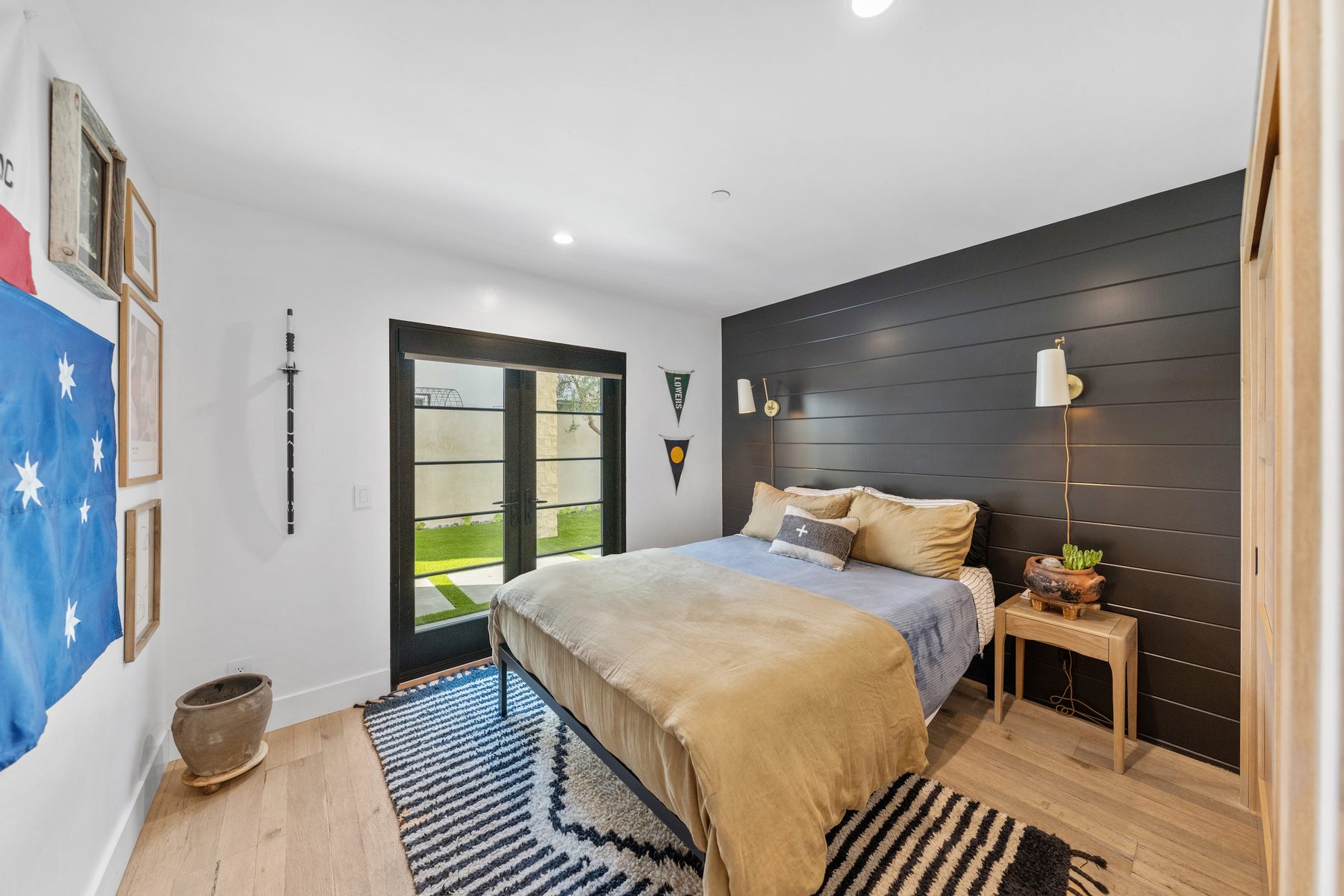 Bedroom with a black shiplap wall, brass sconces and a striped rug