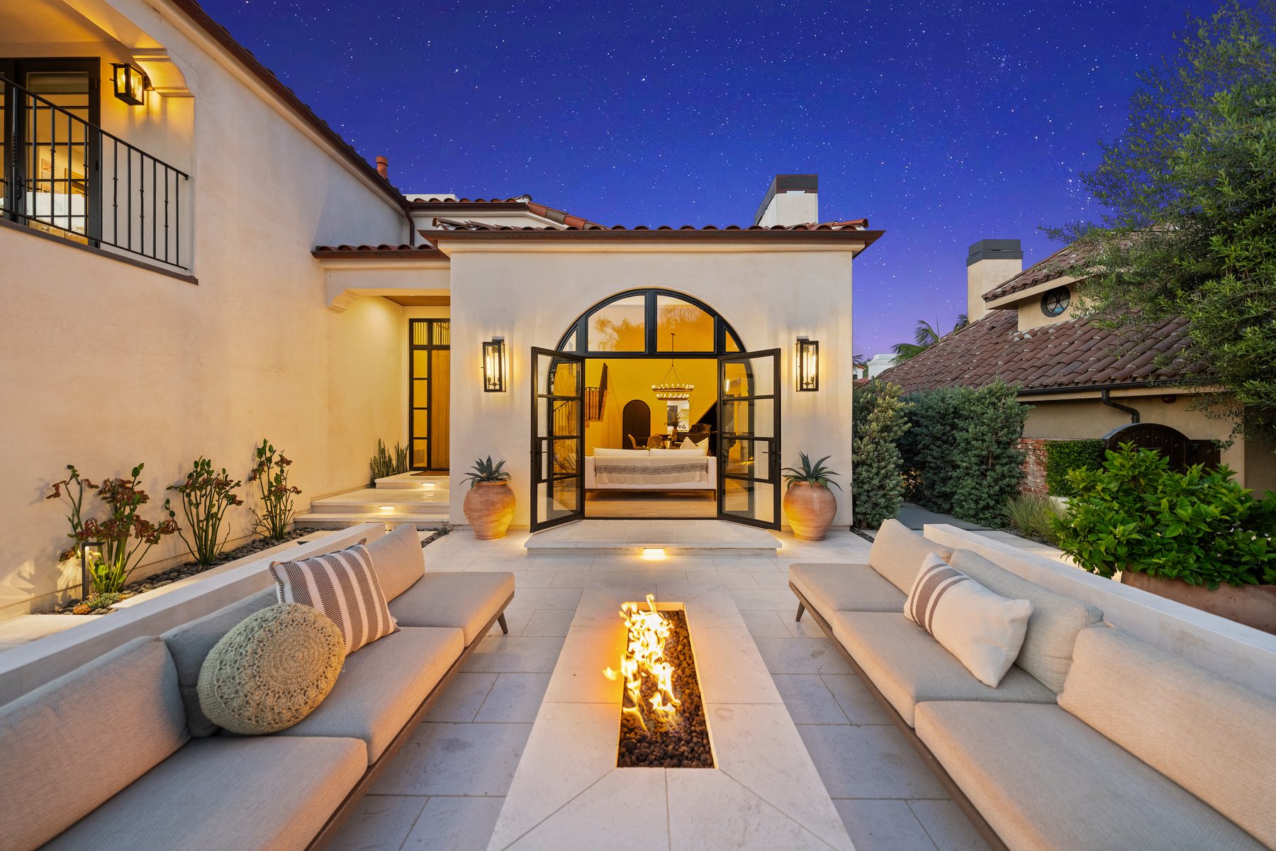 Courtyard at dusk with built-in seating around a linear fire pit and arched steel doors