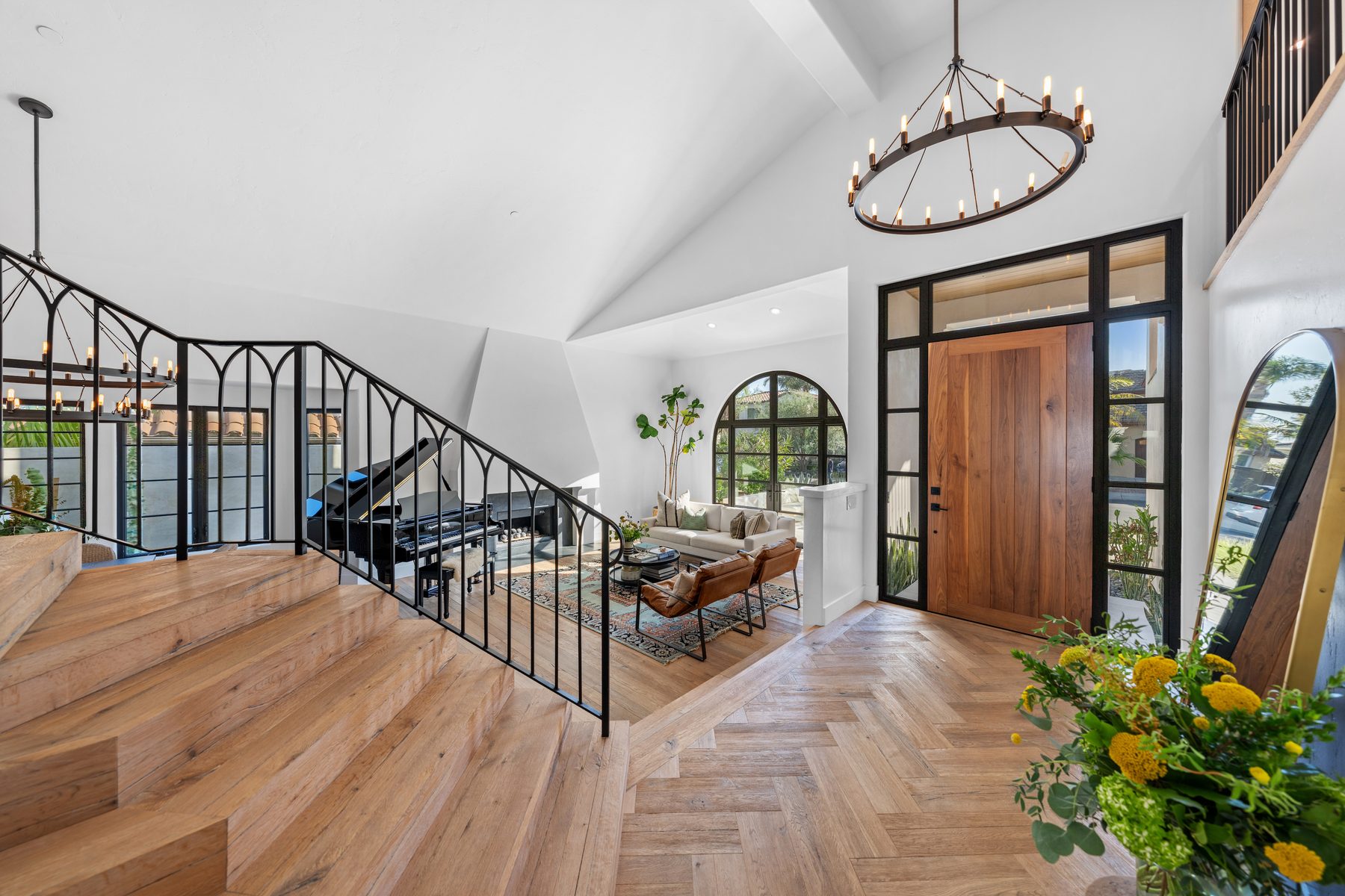 Entry with herringbone oak floor, a walnut front door, iron stair railing and a ring chandelier