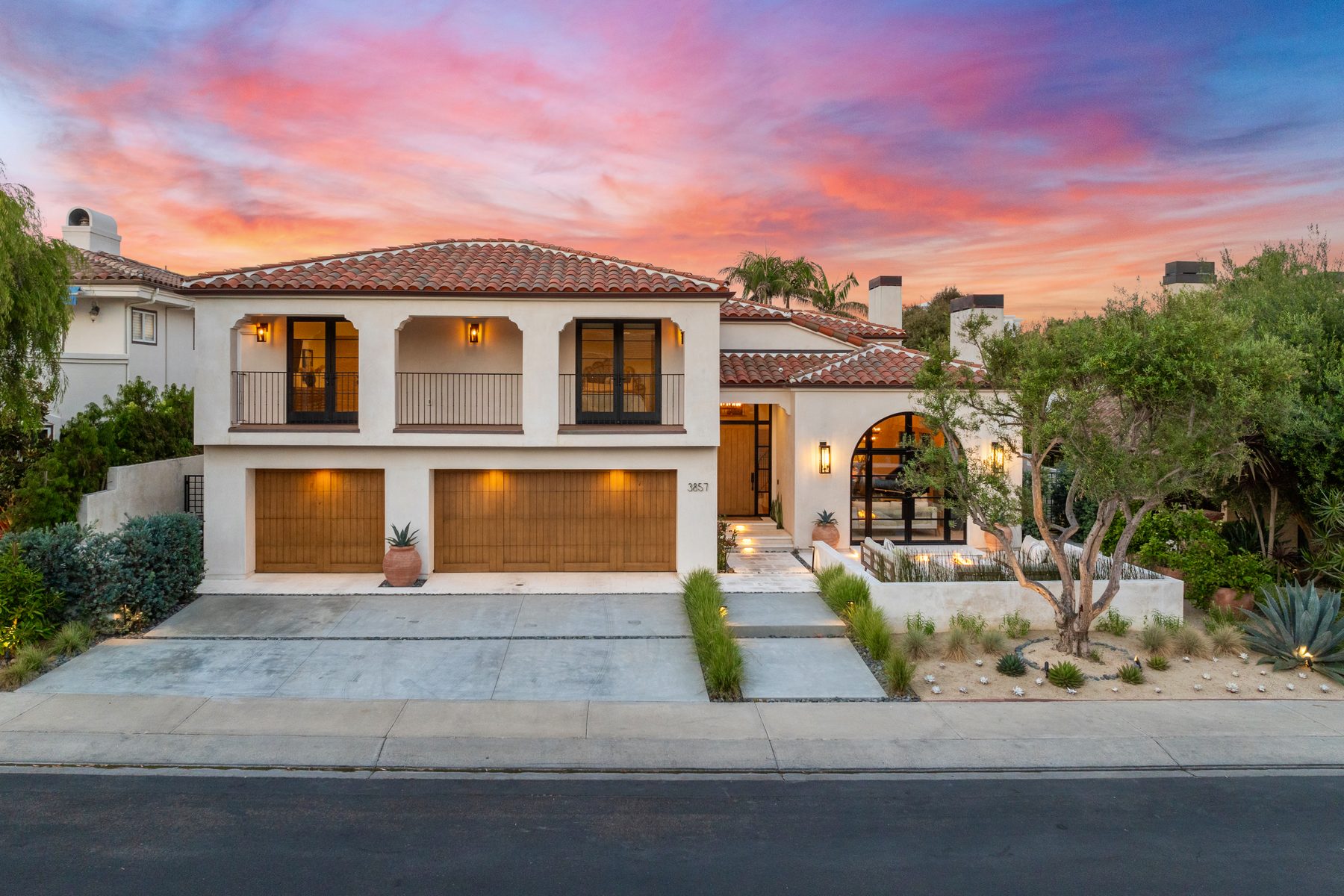 Spanish-style exterior at sunset with a clay tile roof, wood garage doors and an olive tree