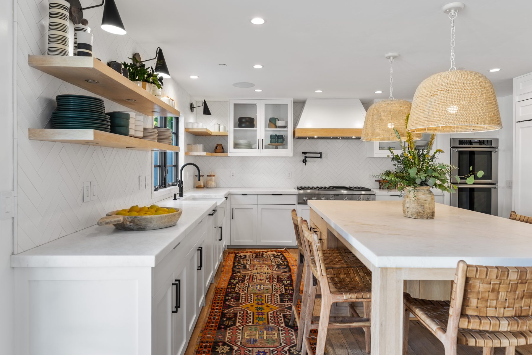 White kitchen with herringbone tile, oak open shelves, woven pendants and a vintage runner