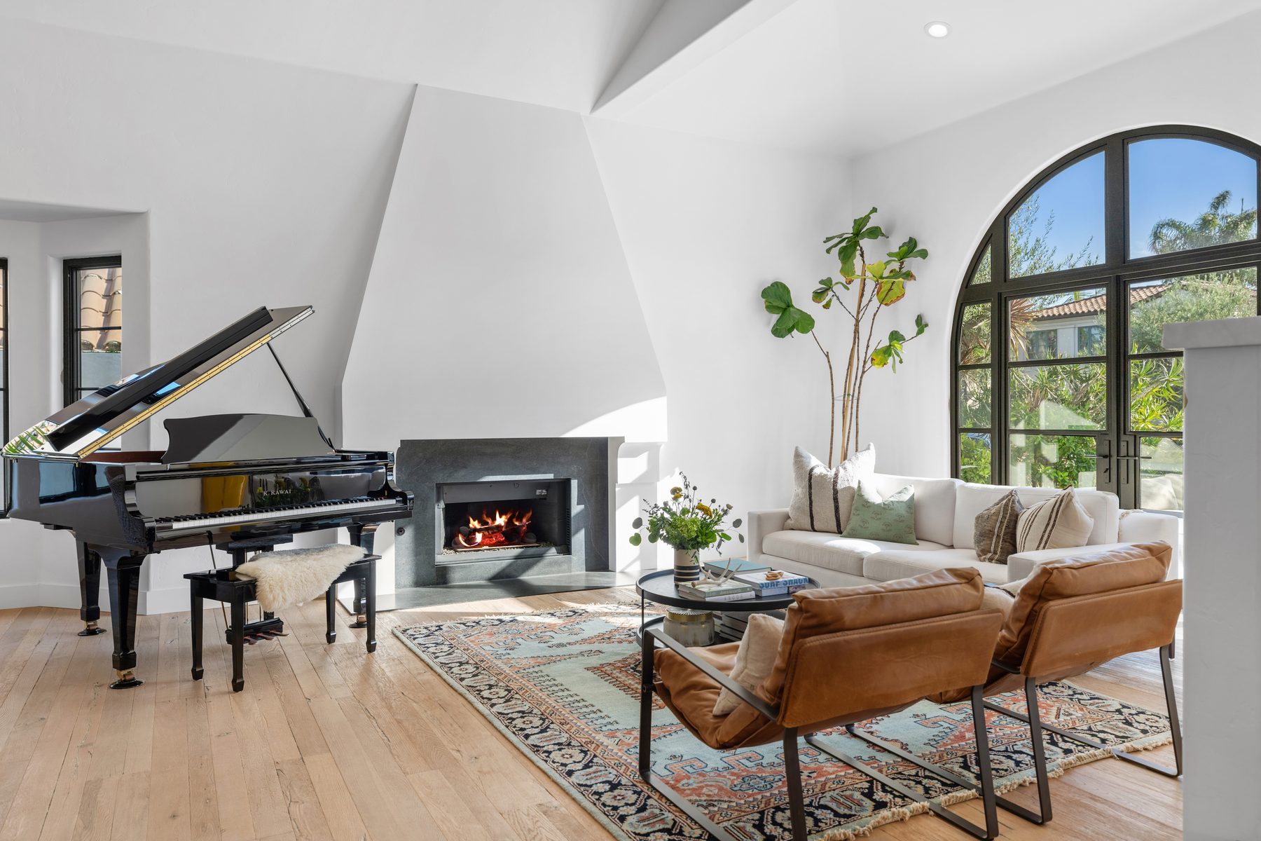 Establo Project living room with a grand piano, a stone fireplace, leather sling chairs and a tall arched steel window