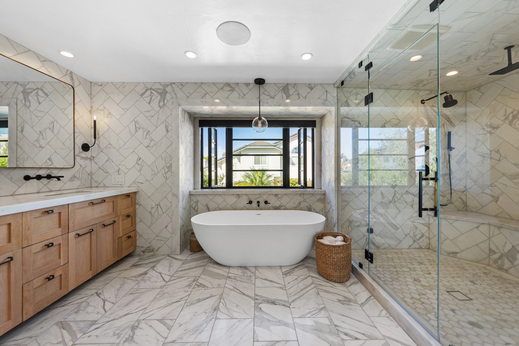 Freestanding tub under a steel window beside a glass-enclosed marble shower