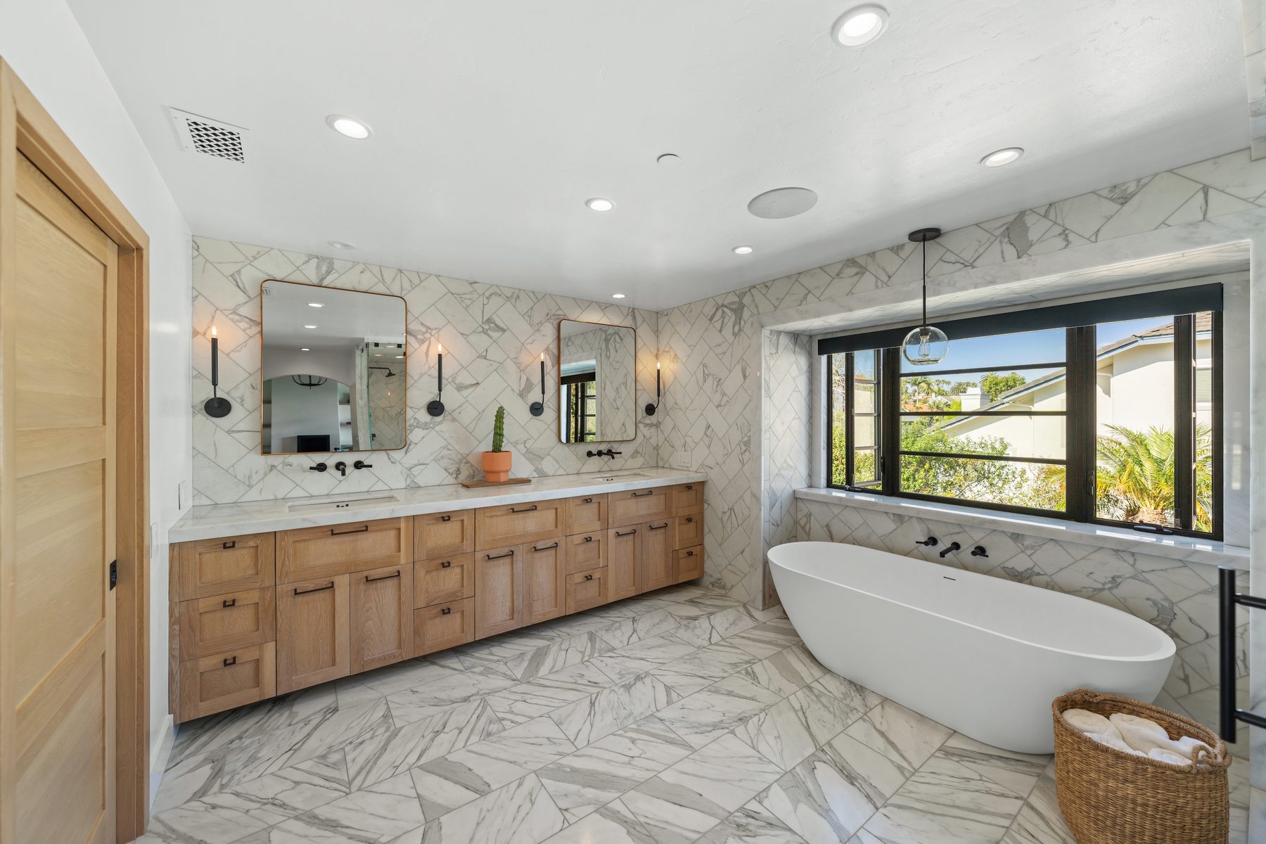 Primary bath with a floating oak vanity, marble herringbone walls and a freestanding tub
