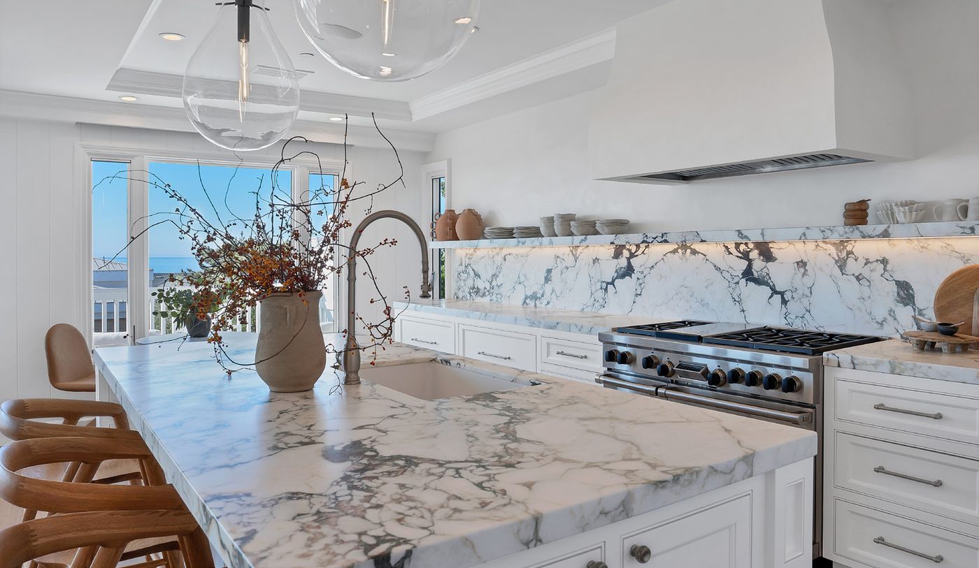 Marble kitchen island with woven stools and an ocean view beyond