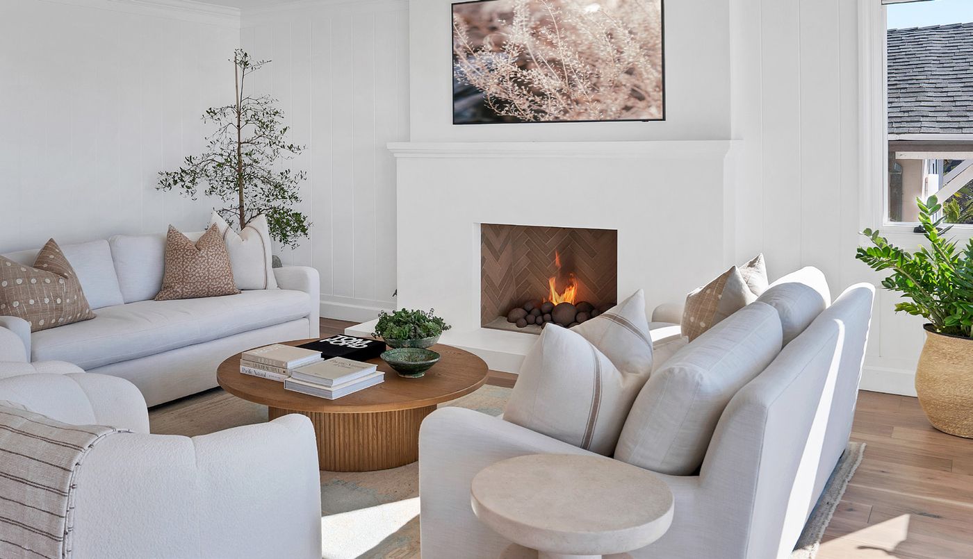 Living room with white sofas around a round wood coffee table and a lit fireplace