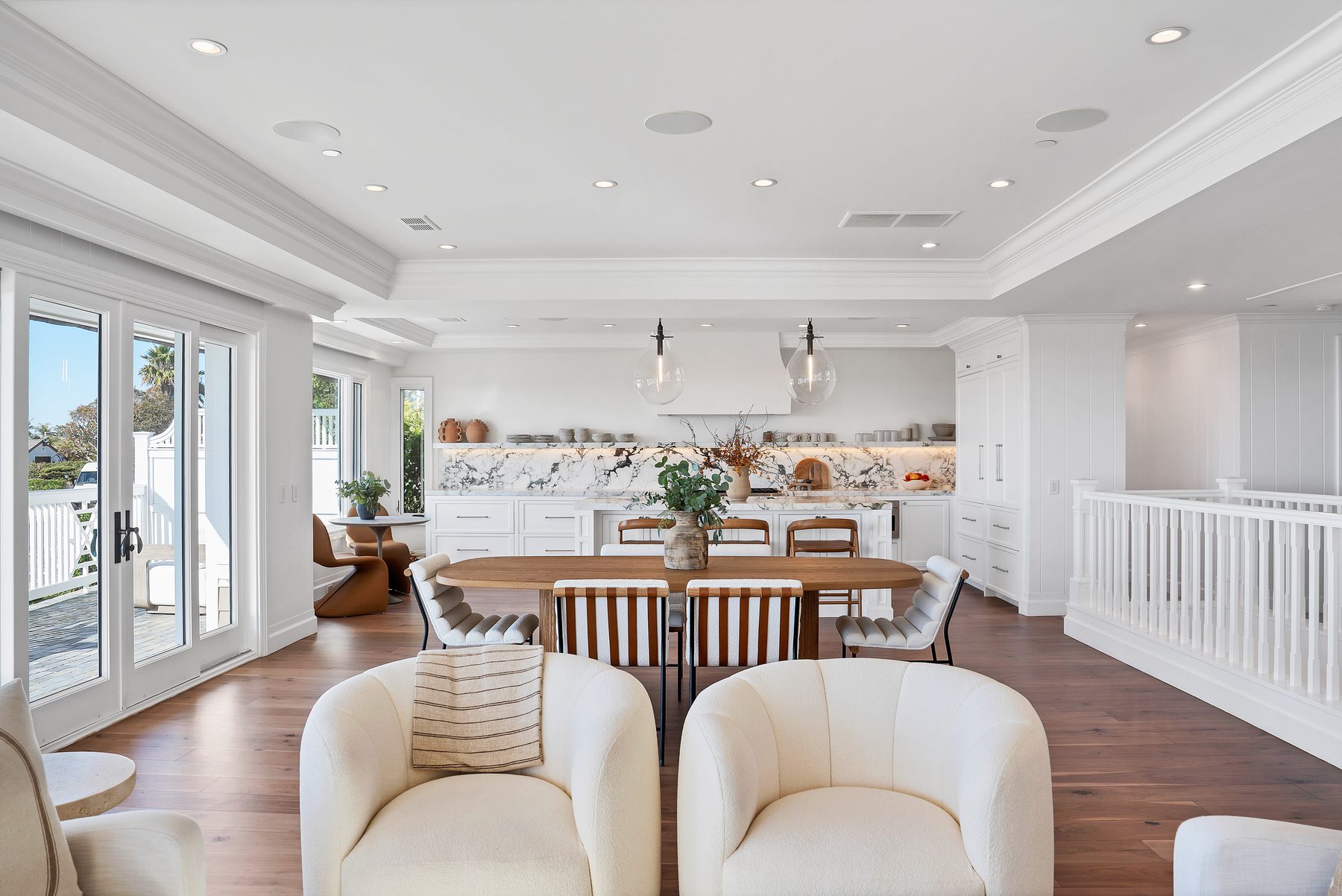 Three Arch Bay great room with an oval wood dining table, glass pendants and a white kitchen with a veined marble backsplash