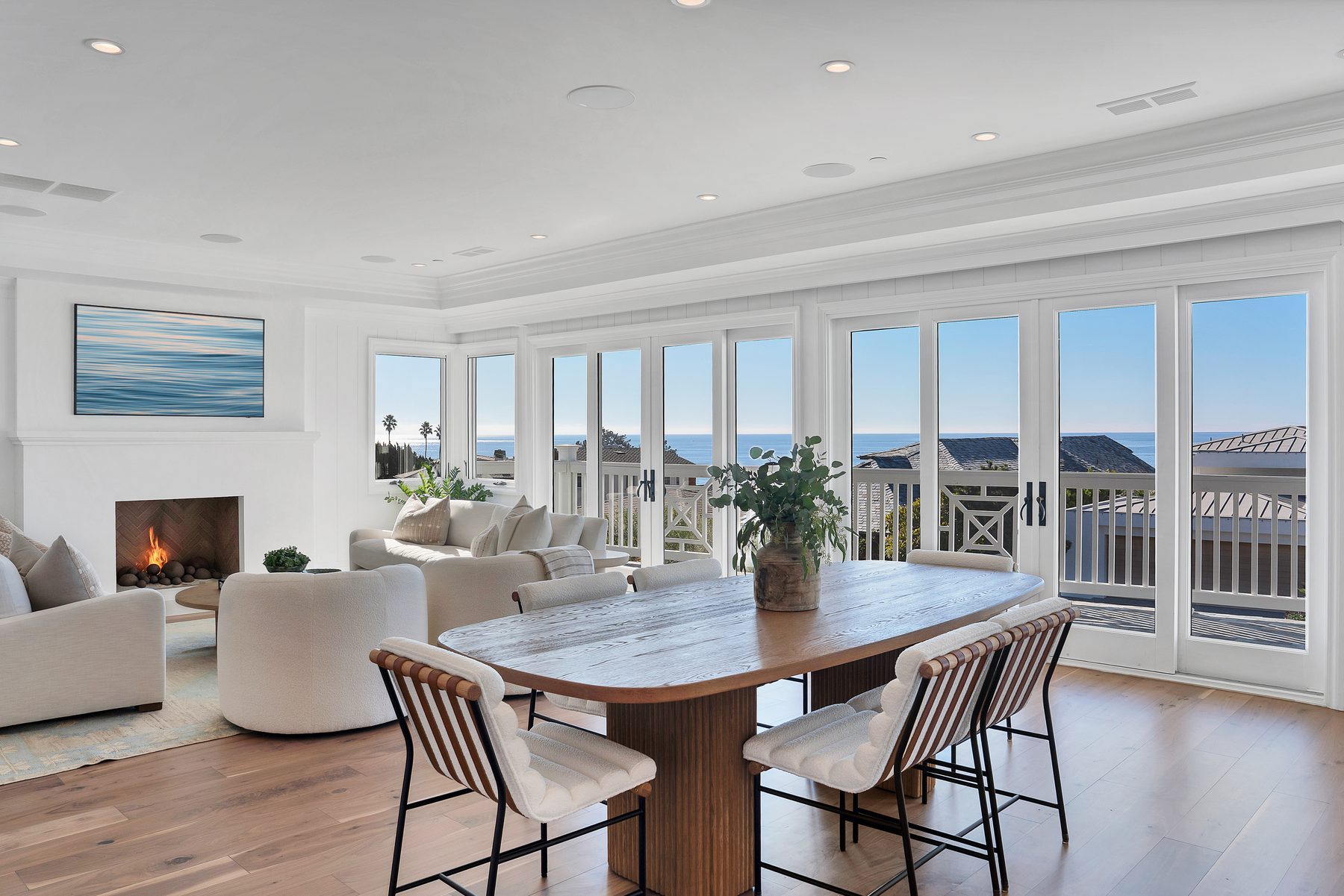 Three Arch Bay dining table with striped chairs, a fireplace seating area and doors open to the ocean