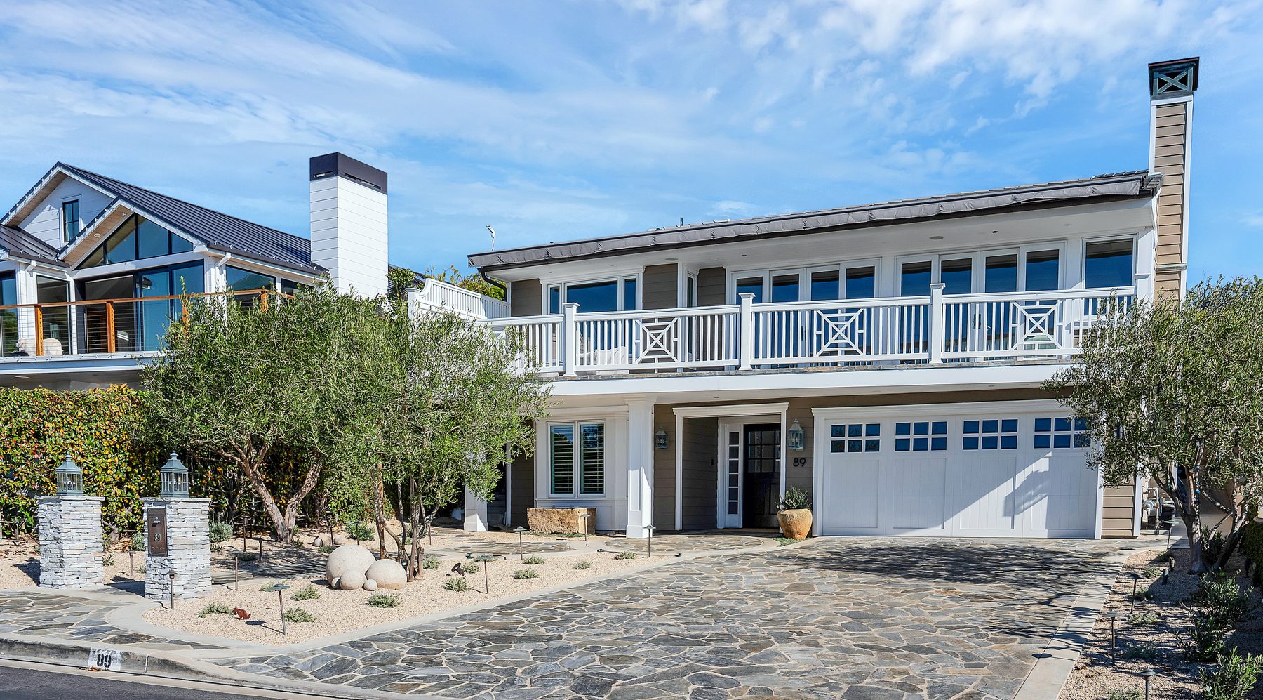 Three Arch Bay exterior: a two-storey coastal home with a white railed deck, olive trees and a flagstone driveway