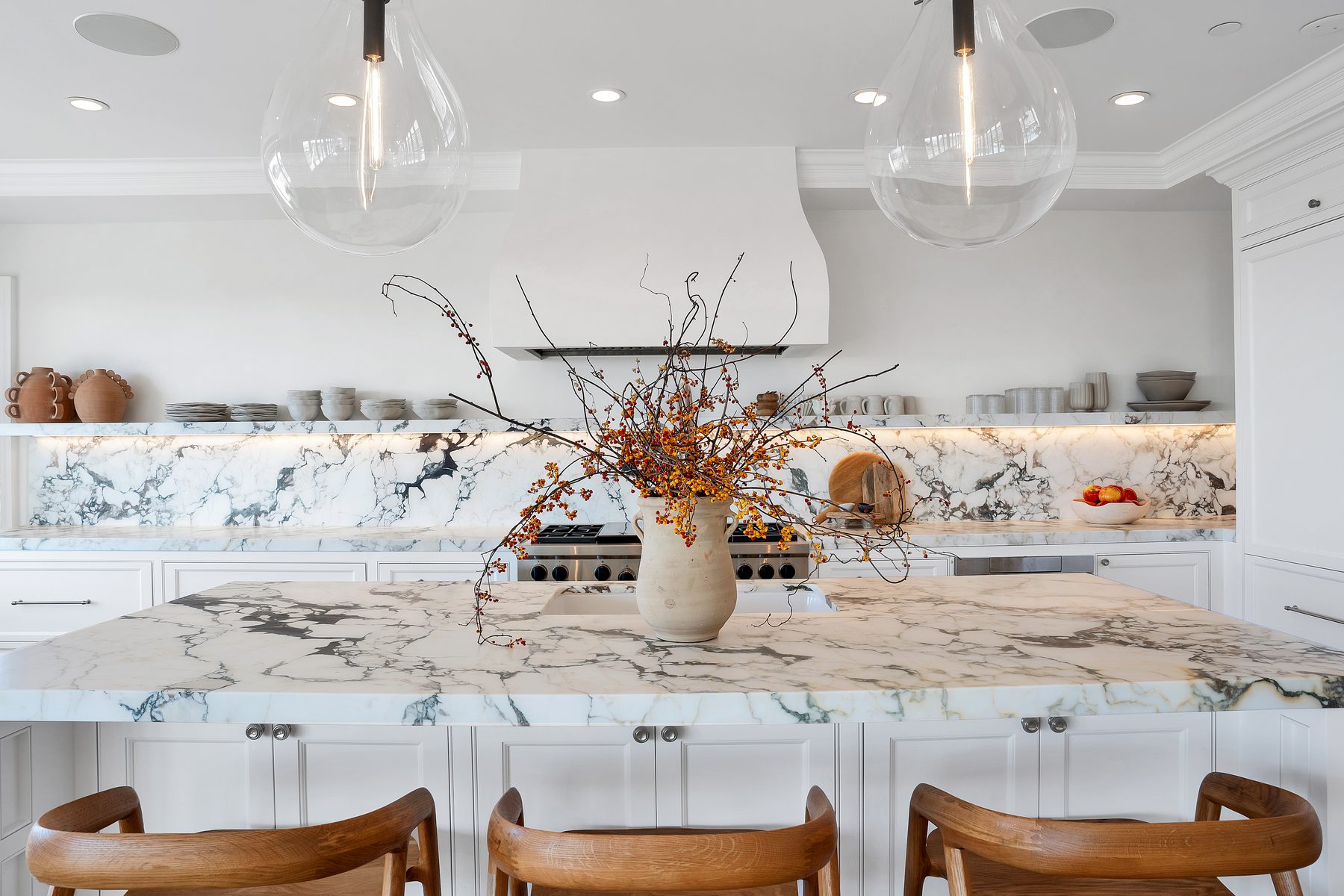 Marble kitchen island with autumn branches in a clay vase, glass pendants above and wood counter stools