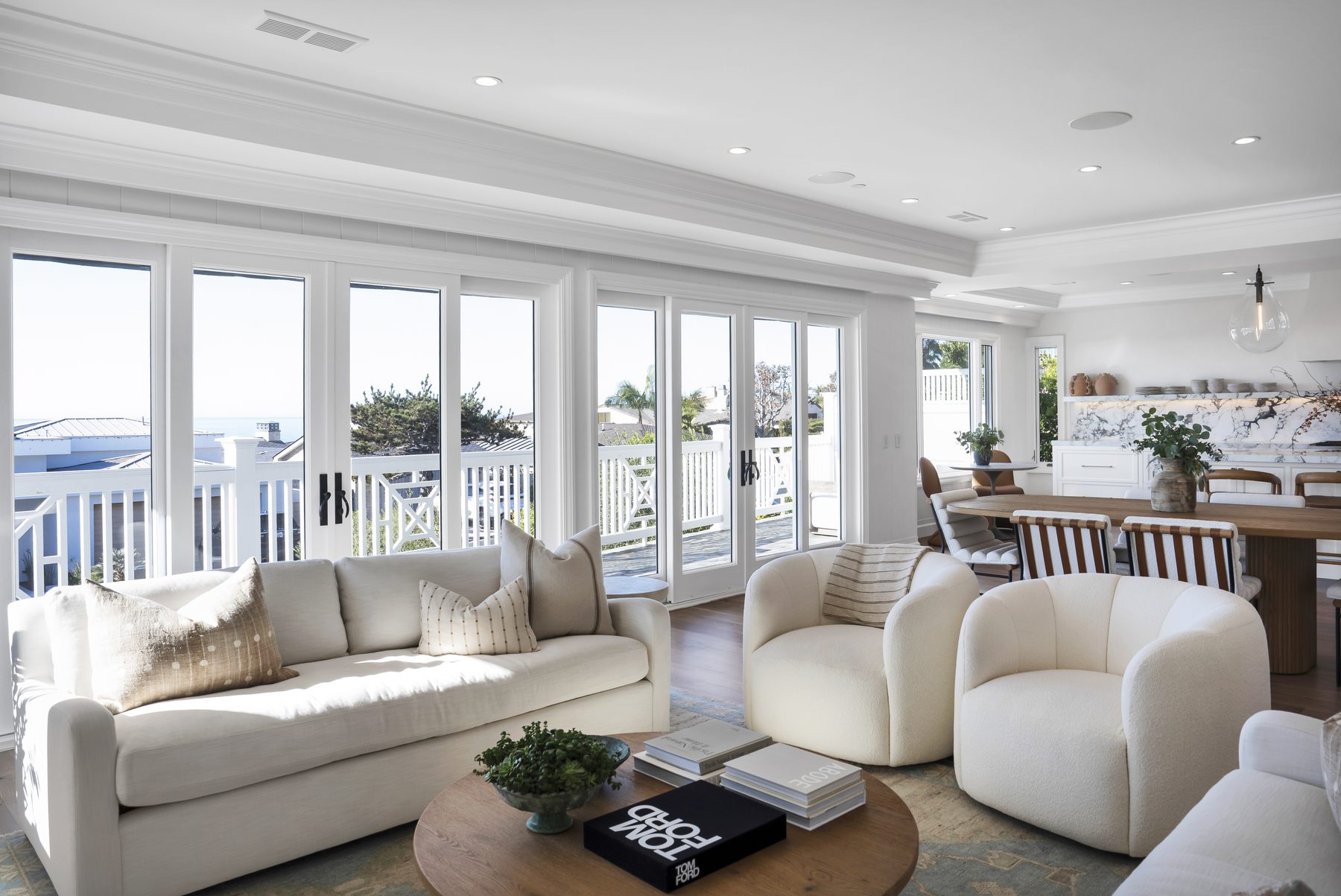 Three Arch Bay living room with a white sofa, boucle swivel chairs and French doors onto an ocean-view deck