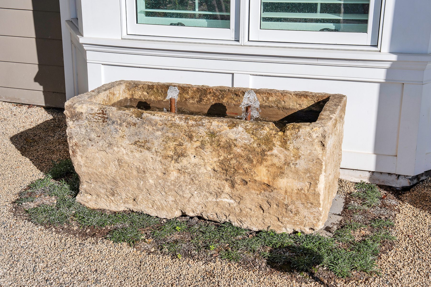 Antique stone trough fountain set in gravel outside the house