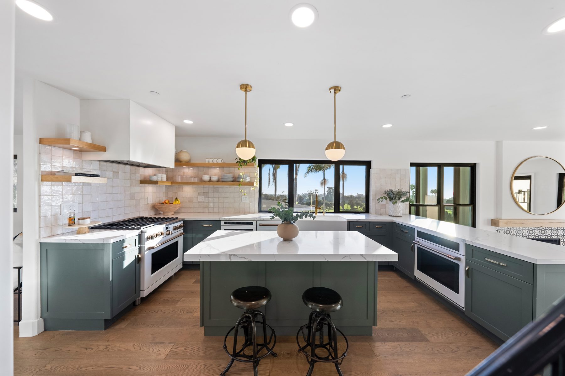 Vista Bahia kitchen with deep green cabinetry, white quartz counters, zellige tile, oak shelves and brass globe pendants