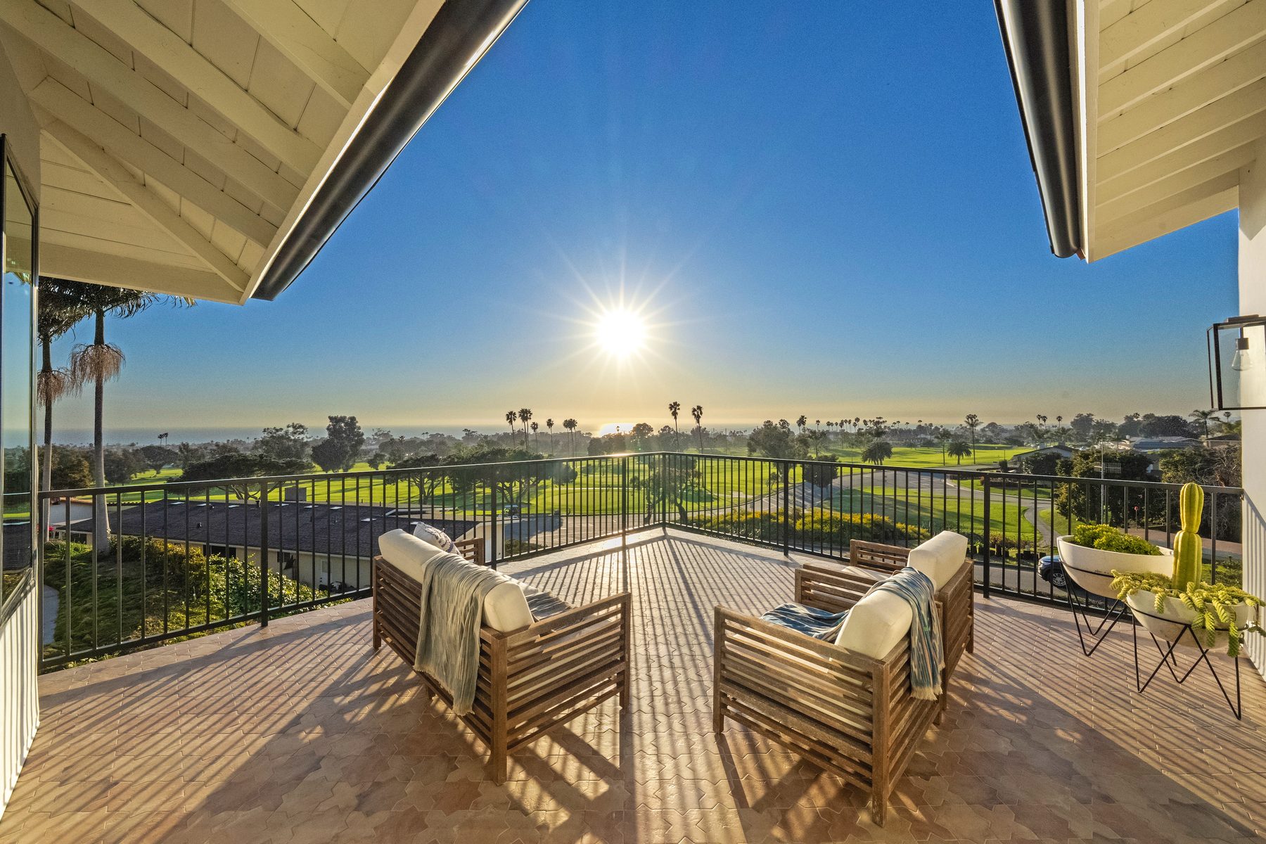 Vista Bahia terrace with two teak lounge chairs facing the golf course and the ocean at sunset